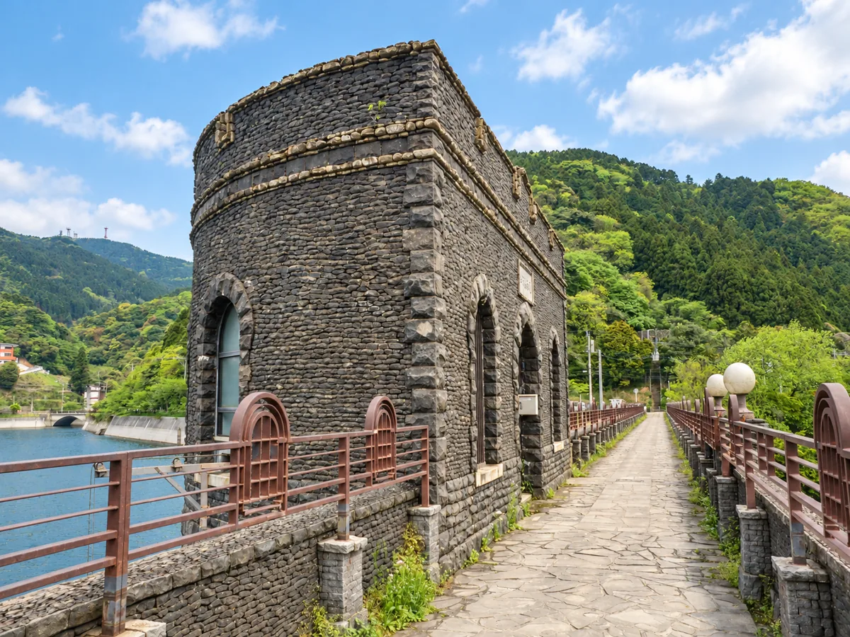 堰堤の上に立つ石張りの取水塔と、アーチ形の窓や水辺へ延びる道