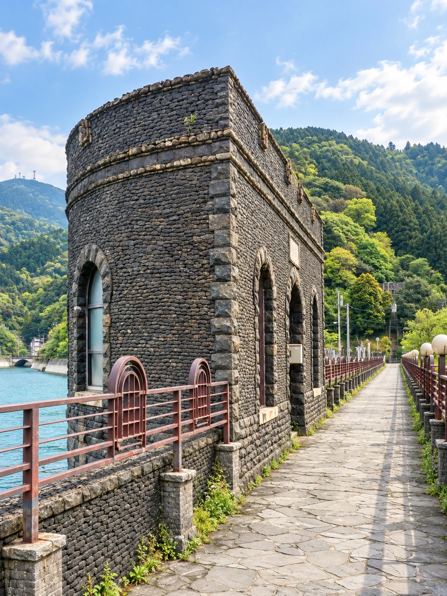 河内貯水池の水辺に建つ石張りの取水塔と、堰堤上に延びる道